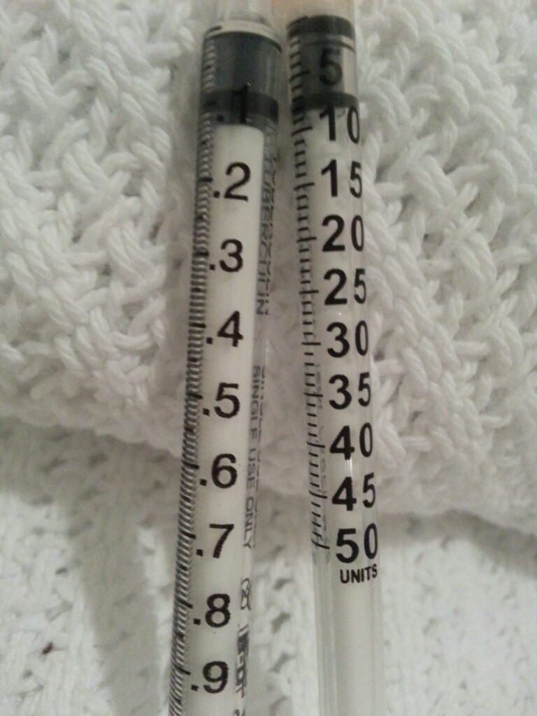 Photograph comparing a syringe marked in insulin units with a tuberculin syringe marked in milliliters.